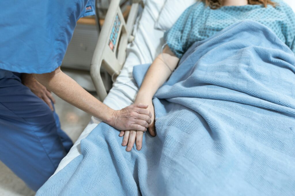 what happens if you become incapacitated? A nurse in scrubs offers comfort by holding a patient's hand in a hospital bed.