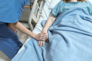 what happens if you become incapacitated? A nurse in scrubs offers comfort by holding a patient's hand in a hospital bed.