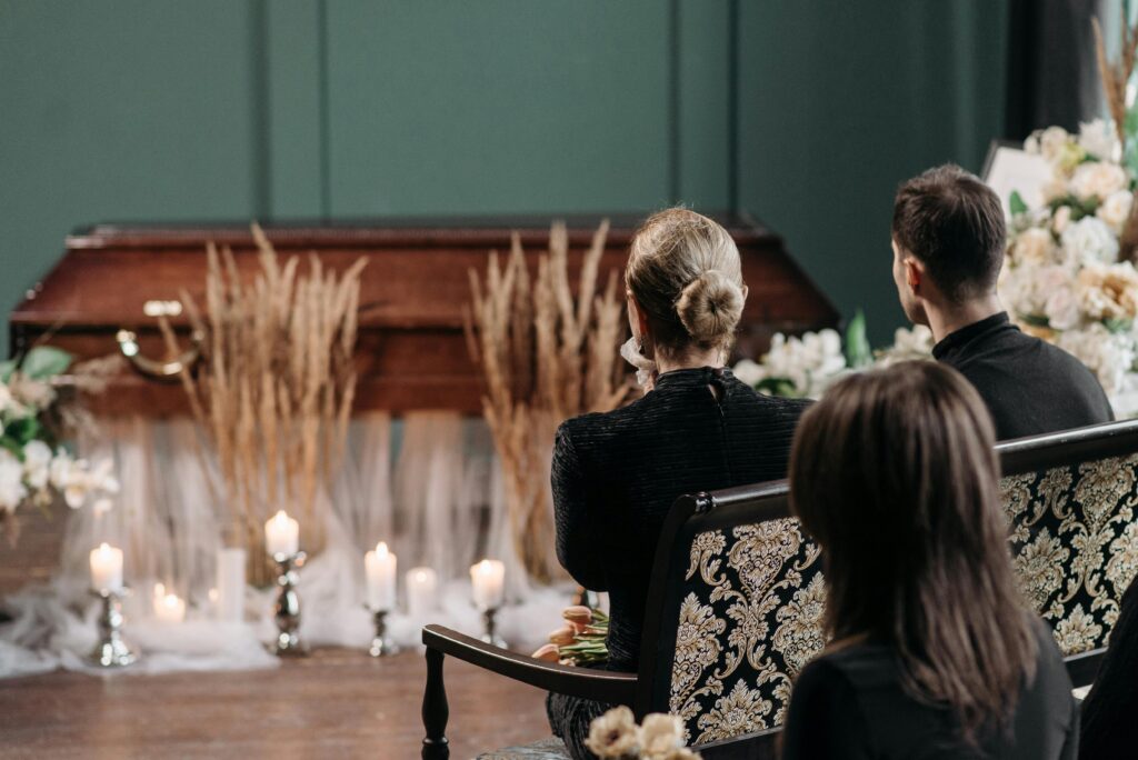 A respectful funeral planning gathering of family and friends at a funeral service indoors, with floral arrangements and candles.