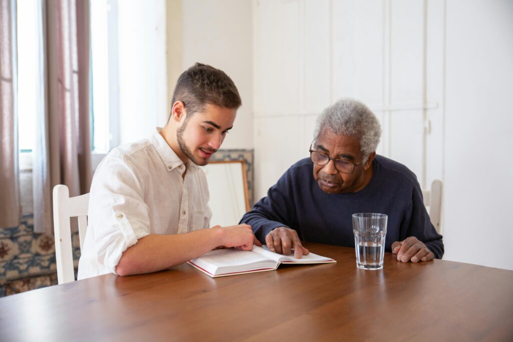 Navigating Alzheimer’s and dementia through legacy planning. A young man and senior sharing a book, fostering connection and learning.