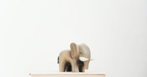 A minimalist scene with a wooden elephant figurine placed on top of stacked books against a light background.